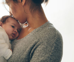 Mother holding newborn kissing head - feature