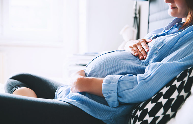 Pregnant woman sitting on couch relaxing with belly - feature