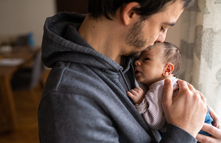 Young father in hoodie holding newborn baby - feature