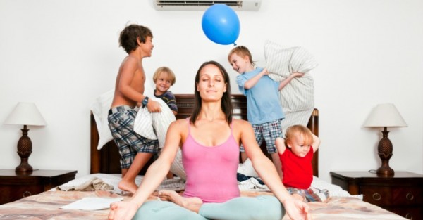 mum sitting cross legged on bed while children jump on bed