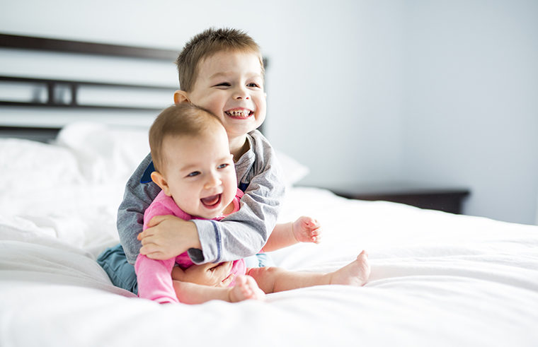 Toddler boy and baby girl hugging on bed - feature