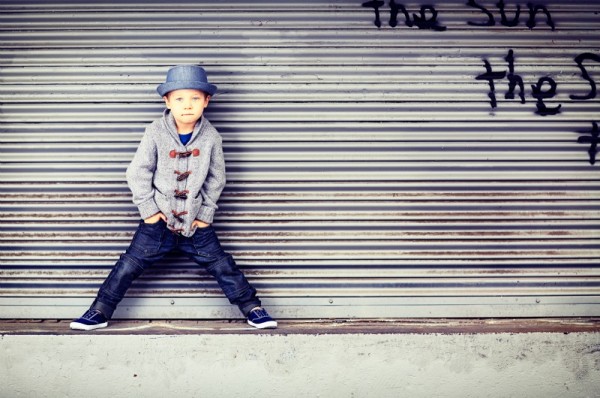 young boy in jeans and cardigan in front of urban graffiti on roller door