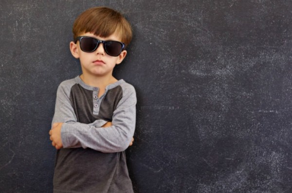 child wearing sunglasses standing in front of grey wall