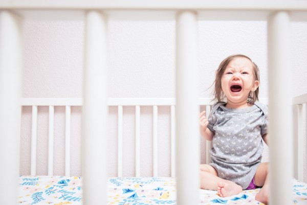 Baby crying and screaming as seen through the bars of her crib.
