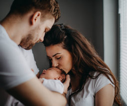 Parents holding newborn baby mother kissing baby head - feature