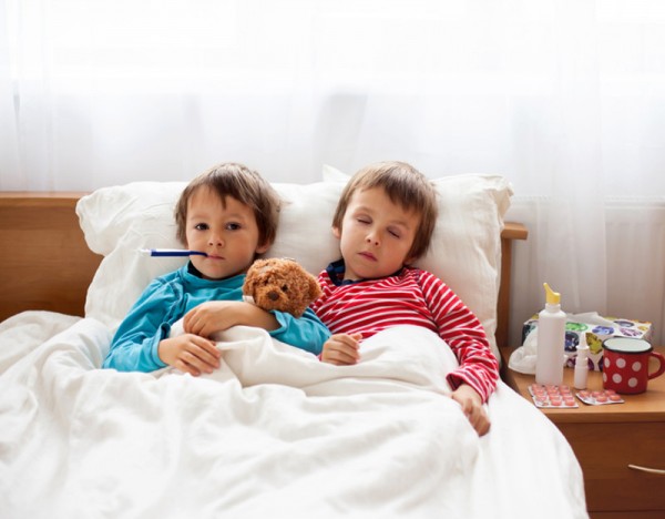 Two sick boys, brothers, lying down in bed with fever, holding teddy bear and resting