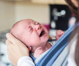 Baby crying in sling with mother - feature