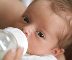 Young baby drinking milk from a bottle - feature