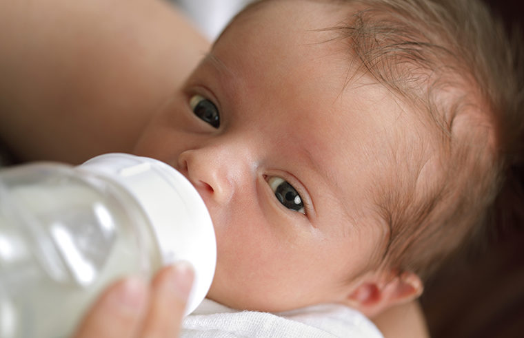 Young baby drinking milk from a bottle - feature
