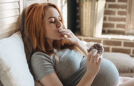 Pregnant woman reclining eating an iced donut