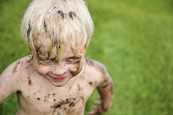 A happy little boy child is smiling as he runs and plays outside on a summer day, while covered in mud and dirt.