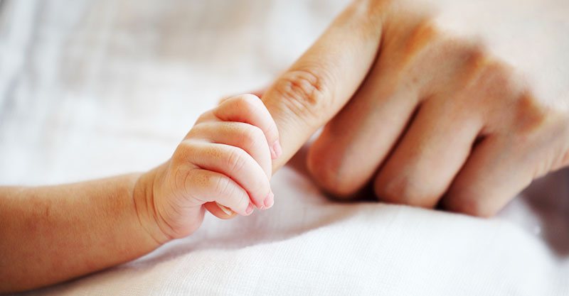 newborn baby and parent holding hands