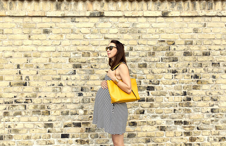 Pregnant woman walking past brick wall - feature