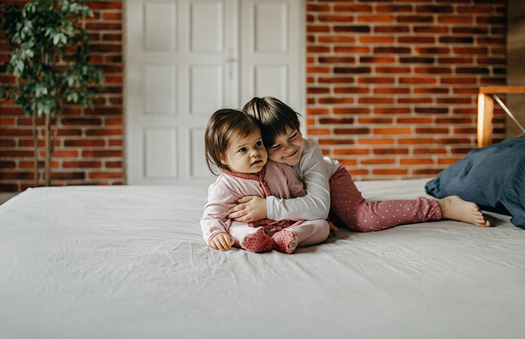 Girl sibling hugging baby sister - feature