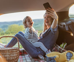 Mother and toddler taking selfies in back of car having picnic - feature