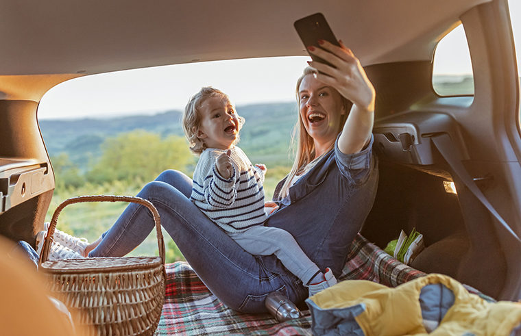 Mother and toddler taking selfies in back of car having picnic - feature
