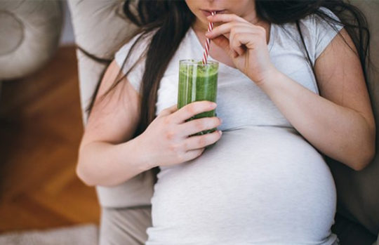 Pregnant woman drinking healthy green juice smoothie