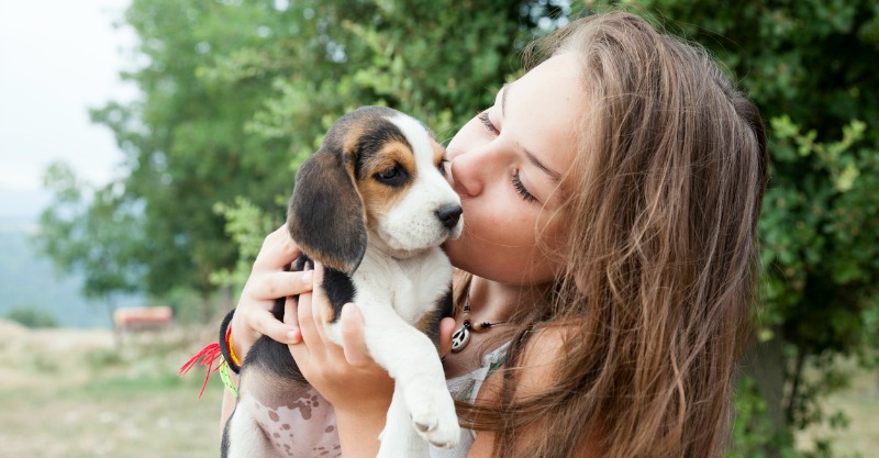young girl kissing her puppy