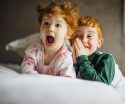 Redheaded brother and sister siblings playing on bed in pyjamas - feature