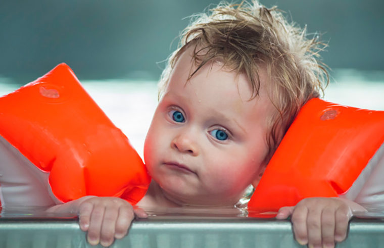Toddler wearing floaties in swimming pool - feature