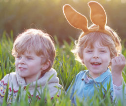 Two happy boys sitting in long grass wearing Easter bunny ears - feature
