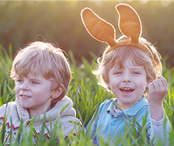 Two happy boys sitting in long grass wearing Easter bunny ears - thumbnail