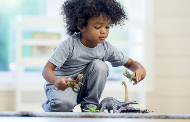 Little boy sitting on floor playing with toy dinosaurs - feature