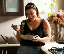 Woman standing in kitchen eating salad - feature