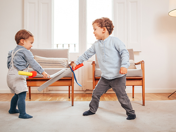 Two young boys playing with swords in the house 