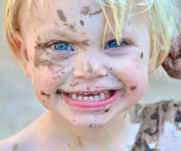 Toddler boy smiling with mud over his face - feature