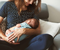Mother breastfeeding newborn baby crosslegged on couch - feature