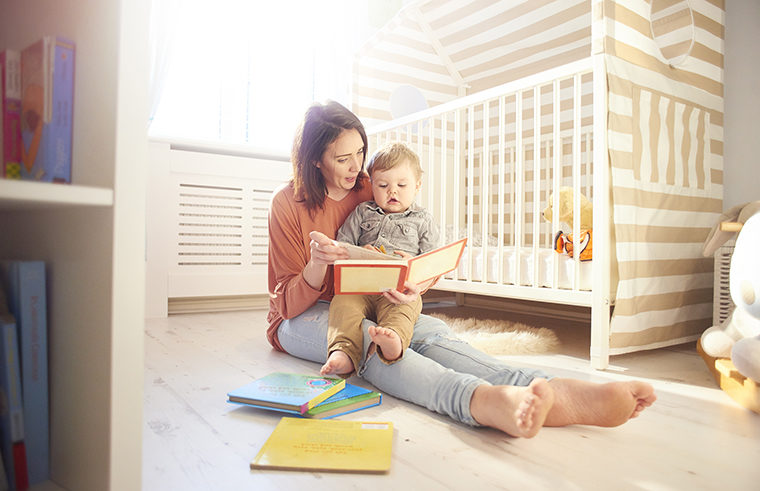 Mother sitting on floor with baby in lap reading books - feature