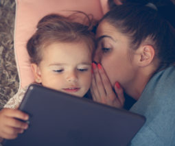 Mother whispering to young girl with ipad tablet - feature