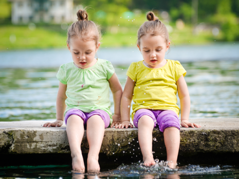 Identical twin girls sitting together with their feet in water