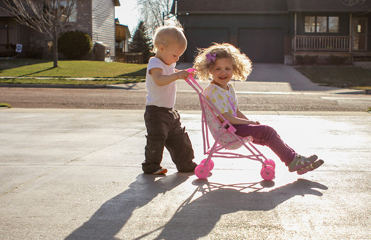 Two sibling girls playing with toy stroller - feature