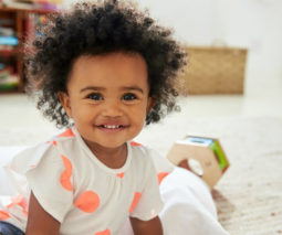 Cute toddler girl with big hair sitting on floor with toys - feature