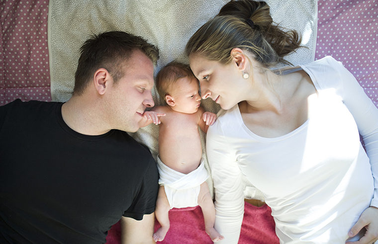 Mother and father lying with newborn baby - feature