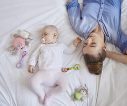 Sleeping mother and sleeping baby sharing bed with toys and dummy - feature