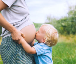 Toddler boy kissing his mother's pregnant belly - feature