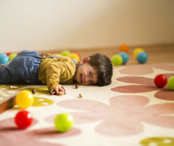Toddler boy lying on rug with toys having a tantrum - feature