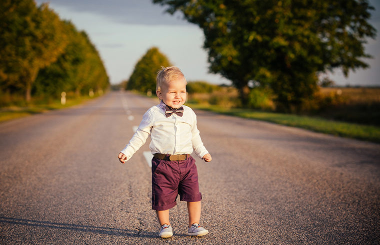 Baby in shorts and bowtie standing on road - feature
