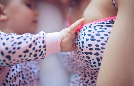 baby reaching out to breast for feeding - feature