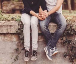 Couple sitting on wall holding hands - feature