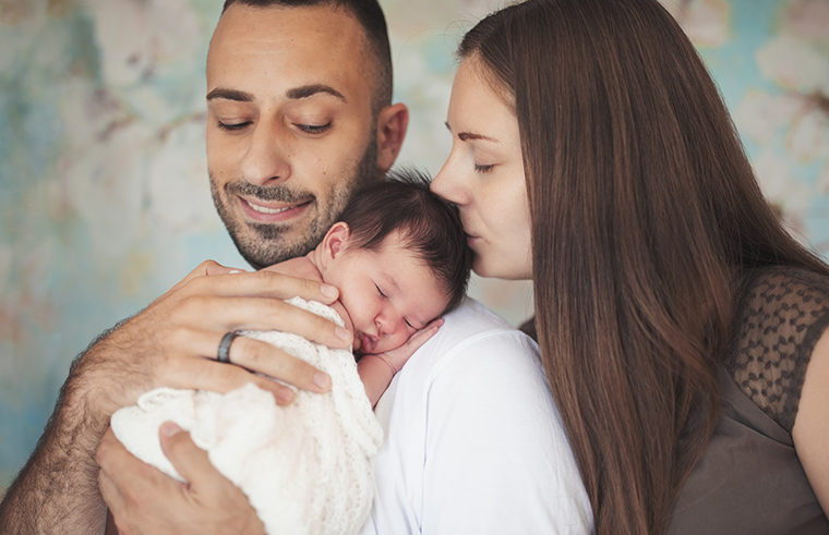 Father holding newborn baby on shoulder mother kissing baby - feature