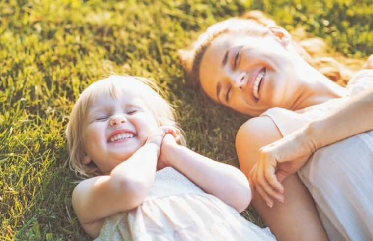 Toddler girl lying on grass with aunt or mother