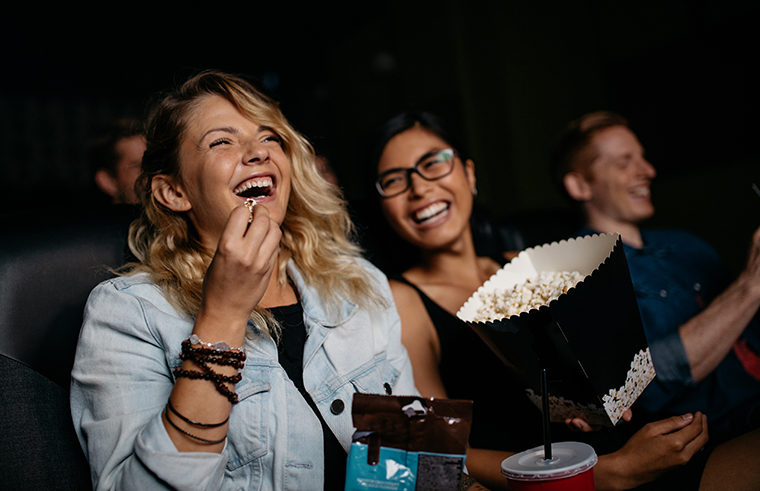 2 women friends laughing at the movies with popcorn - feature