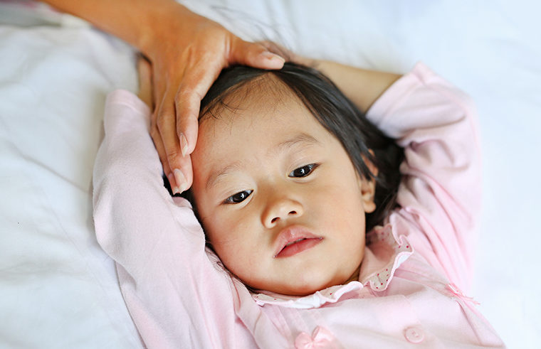 Asian girl toddler in bed sick mother's hand on head - feature