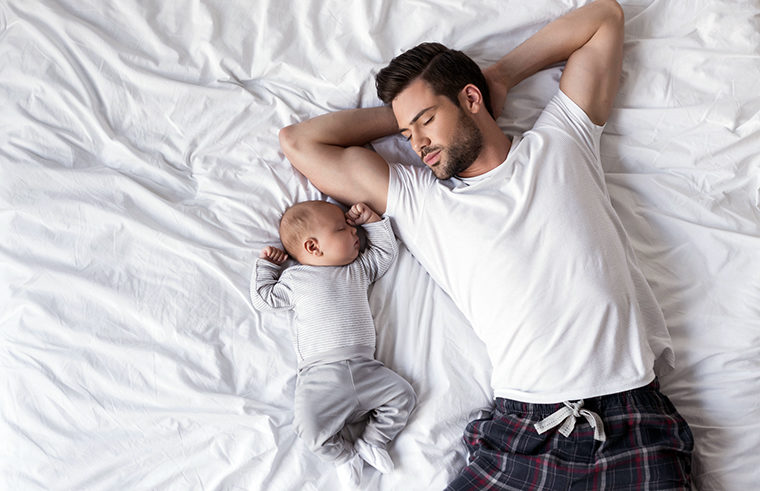 Father and baby asleep together on bed - feature