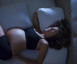 Pregnant woman lying on bed with sore back- feature