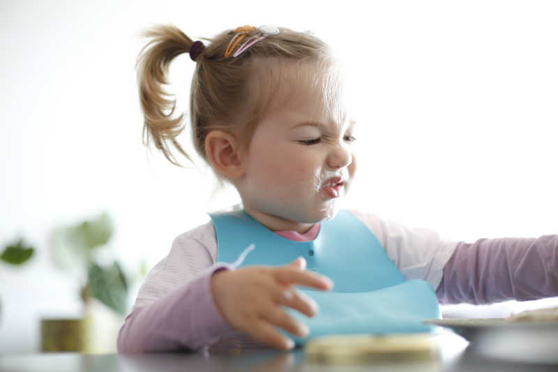 toddler girl picking at food making a funny face